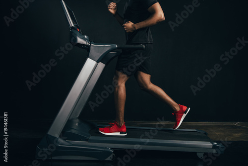 cropped shot of african american sportsman running on treadmill on black