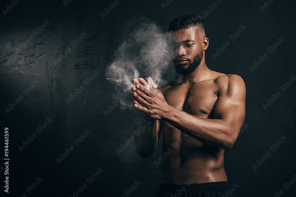 young bare-chested african american sportsman applying talcum powder on hands on black