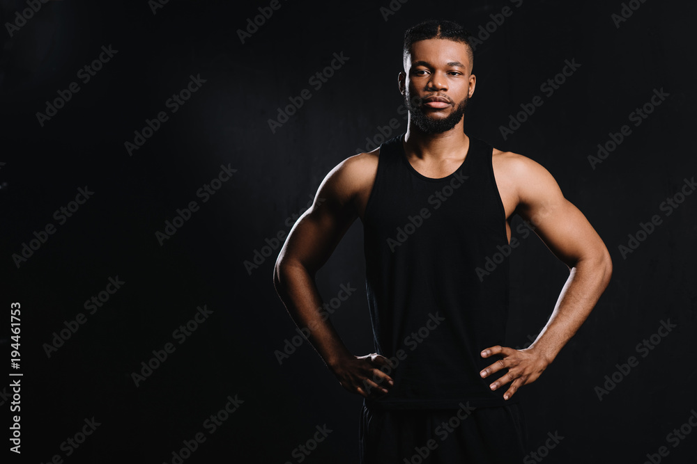 confident african american sportsman standing with hands on waist isolated on black confident african american sportsman standing with hands on waist isolated on black