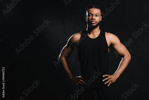 confident african american sportsman standing with hands on waist isolated on black