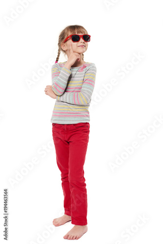 Child girl in sunglasses standing in full length looking to side thinking, isolated on white background