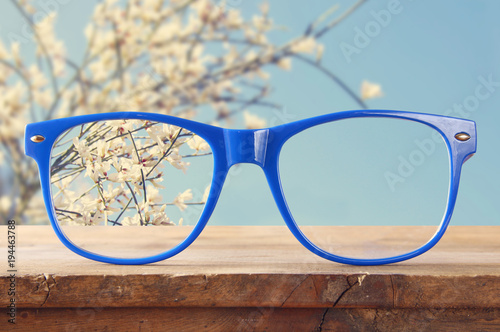 hipster glasses on a wooden rustic table in front of white flowers.
