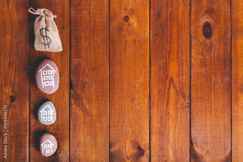 Fototapeta premium Three houses drawn on stones over brown wood with money sack