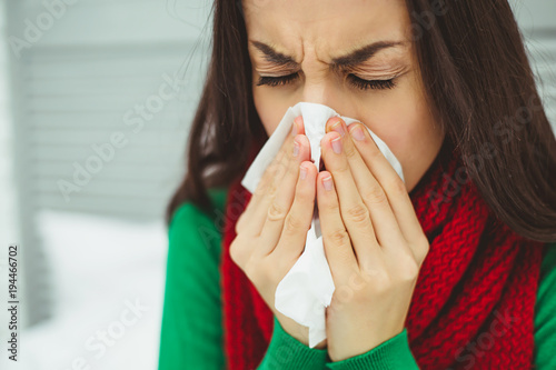 Close up portrait of a young sick woman with a runny nose in a red scarf lying on the bed at home and treated. The concept of health and disease.