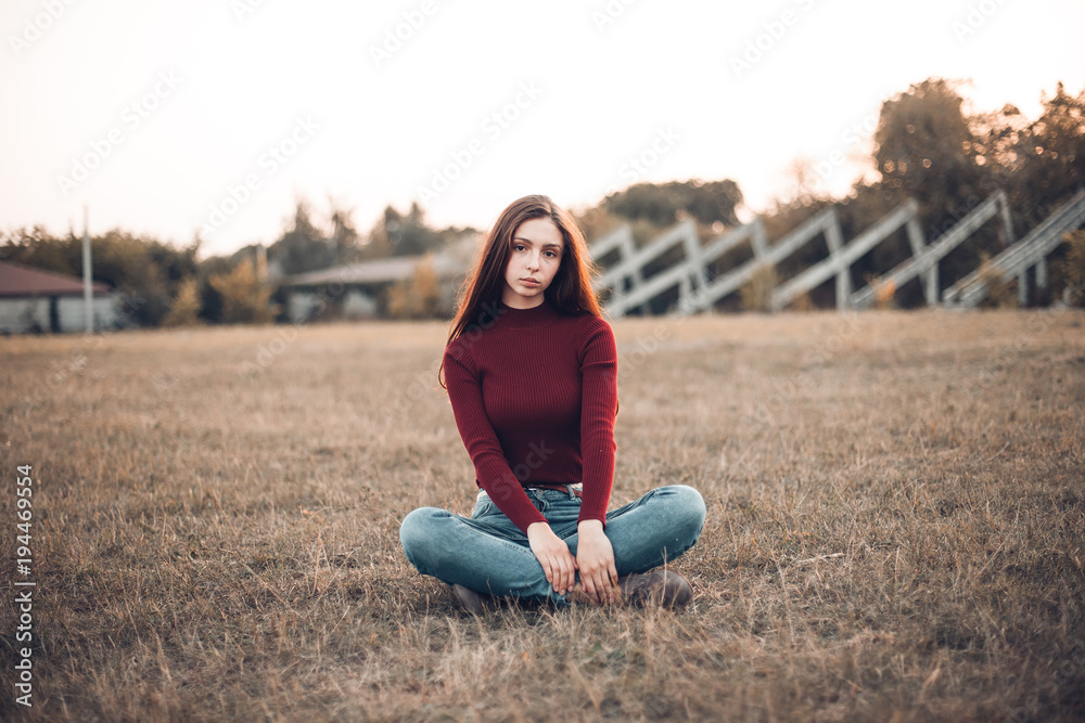 A beautiful young woman is sitting on the field
