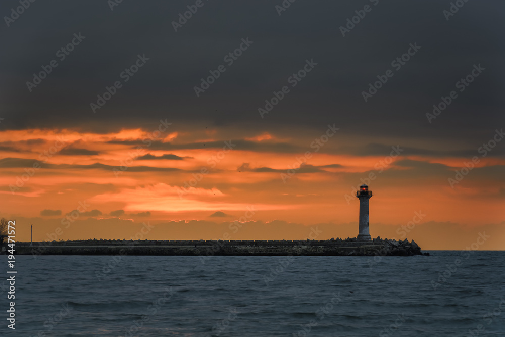 seascape of a Lighthouse at sunrise against a vibrant orange sky.