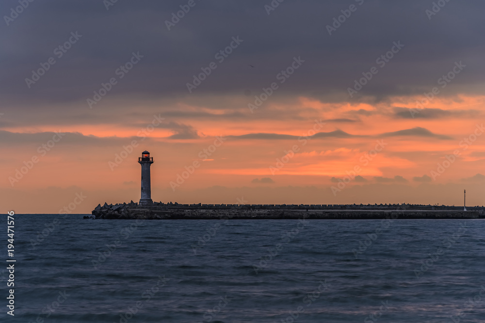 seascape of a Lighthouse at sunrise against a vibrant orange sky.