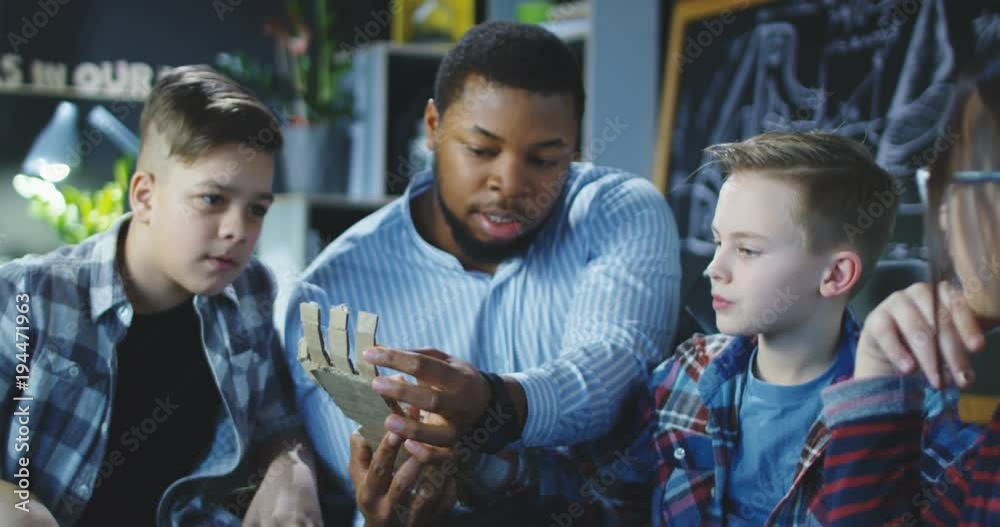 Black man teaching group of children in club and exploring robotic cardboard arm. Movement 4K shot on Red cinema camera.