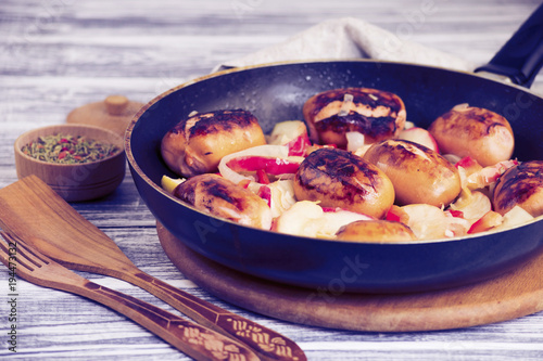 Fried pork sausages with apples and onions in a frying pan