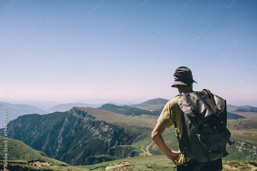 Young hipser man with backpack enjoying mountain view on bright sunny day. Hiker on mountain background. Empty cloudless sky. Young hipser man with backpack enjoying mountain view on bright sunny day. Hiker on mountain background. Empty cloudless sky.