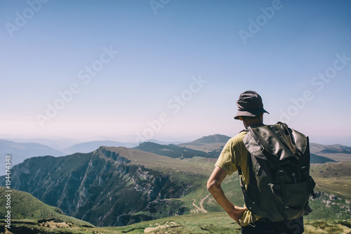 Young hipser man with backpack  enjoying mountain view on bright sunny day. Hiker on mountain background. Empty cloudless sky.