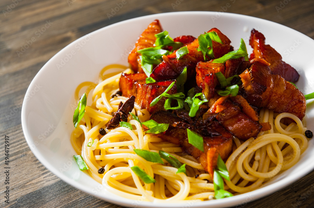 Boiled spaghetti with fried small pieces of meat on a wooden background