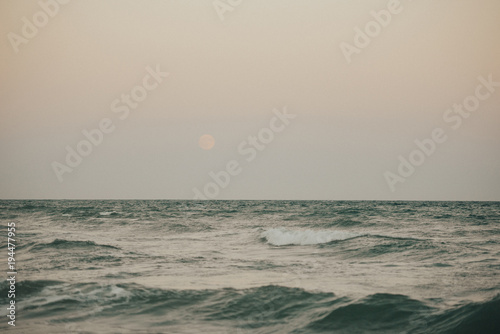 Mediterranean sea with emerald color in the evening with the moon on the rose sky in the Cullera. Valencia Spain