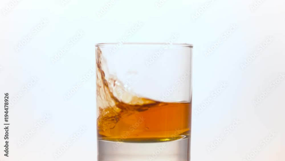 Ice cube falling into a glass of whiskey Ice cube falling into a glass of whiskey