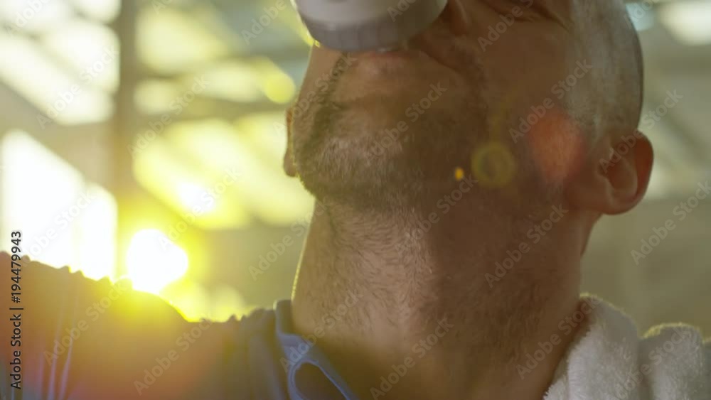 Close up tracking shot of mature man drinking water from bottle after workout, looking at camera and smiling Close up tracking shot of mature man drinking water from bottle after workout, looking at camera and smiling