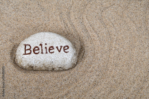 close up of stone with believe text in raked beach sand pattern