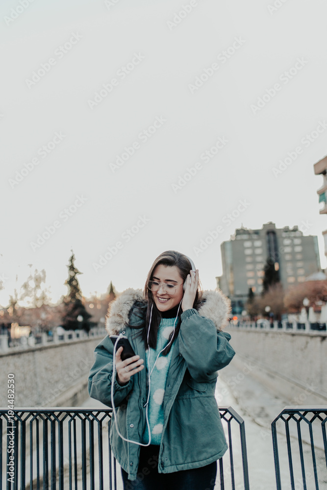 Beautiful woman with glasses listening to music on the street. Beautiful woman enjoying music in the park. Young man listening to music on his headphones