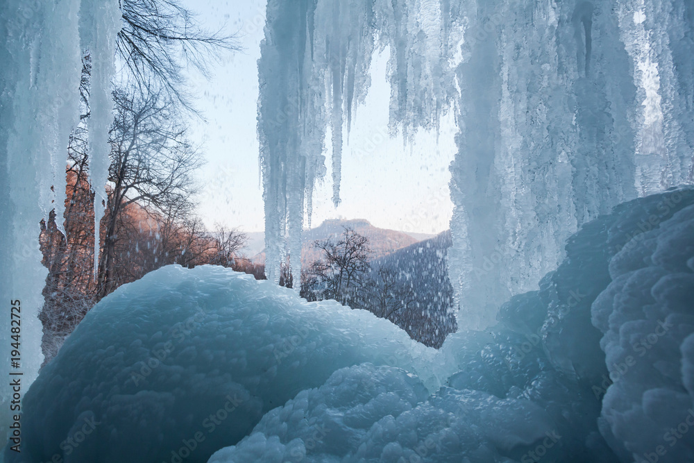 Fototapeta premium Bad Urach Wasserfall mit Eis und Blick auf die Burgruine Hohenurach. In der Eishöhle unter den Eiszapfen.