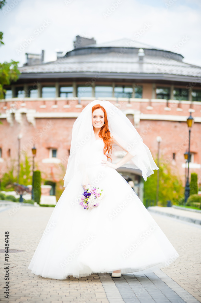Fototapeta premium Beautiful red haired bride perfect style. Wedding hairstyle make-up luxury wedding dress and bride's bouquet.