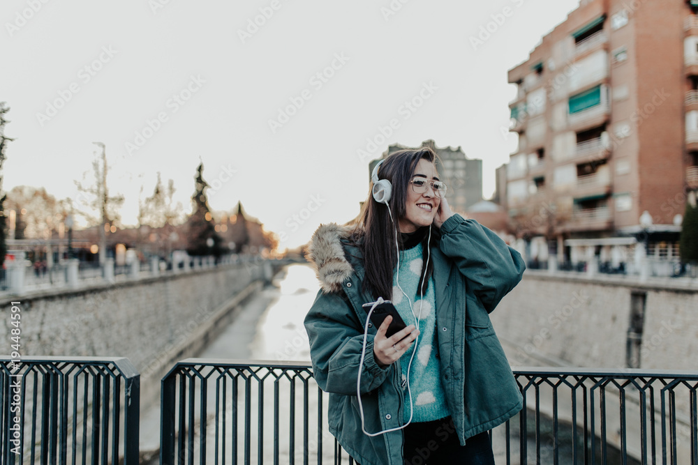Beautiful woman with glasses listening to music on the street. Beautiful woman enjoying music in the park. Young man listening to music on his headphones