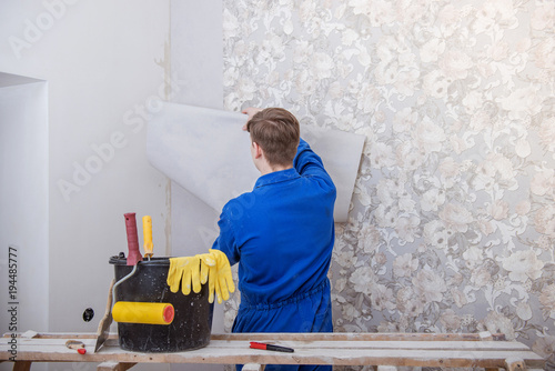 Young worker making repair in room, wallpapering on wall
