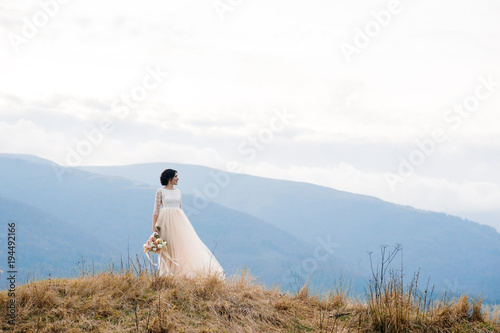 Gorgeous bride with bouquet in hand with mountain landscape on background