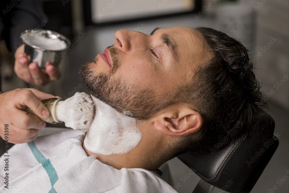 Fototapeta premium Hairdresser shaving his beard with a razor to a client