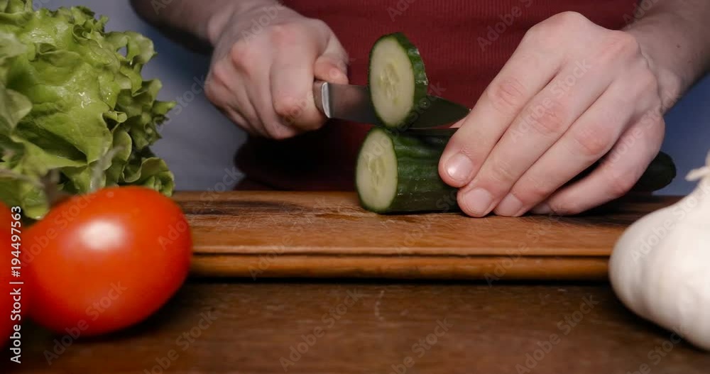 Kitchen table with vegetables, cucumber, tomato, green salad, garlic and knife.