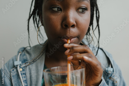 Young woman drinking cold pressed juice against simple backgroun