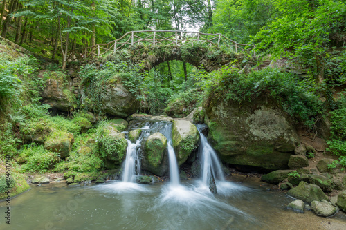 Amazing paradise waterfall in colorful european forest with stone bridge crossing