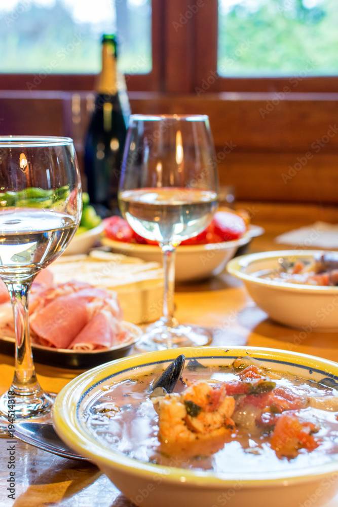 Italian dinner with seafood soup, sliced prosciutto, white wine, and vegetables.