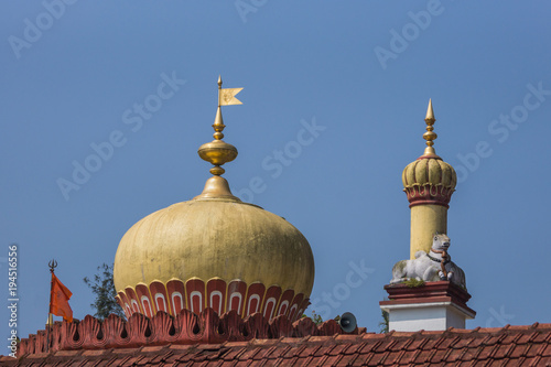 Madikeri, India - October 31, 2013: Shree Omkareshwara Temple. Short turret and bull plus Top gold-yellow dome with metal flag and framed by maroon roof edge on top of the central sanctuary,