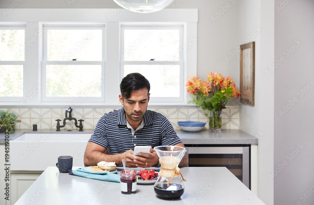 Hispanic man texting at home while eating breakfast Hispanic man texting at home while eating breakfast
