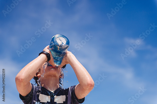 Boy drinking from a large water bottle at the beach in summer