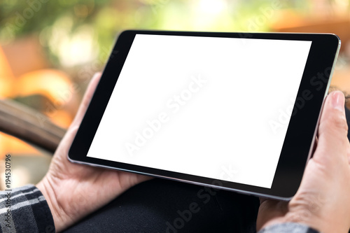 Mockup image of hands holding black tablet pc with blank white screen with blur green nature background