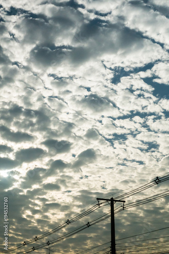 Sky full of fluffy cloud with sun light in daytime and with electricity powerling silhouette in foreground