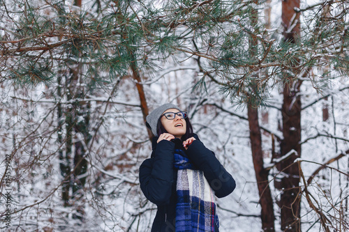 cute girl in glasses under pine branches with snow in winter in the forest