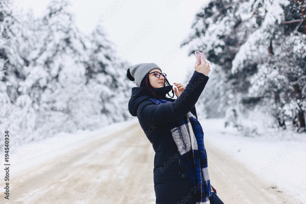 A pretty girl makes a selfie in the middle of a snowy forest road