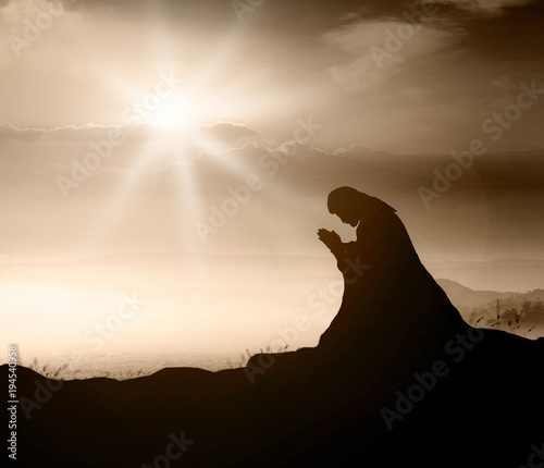 Miracle salvation concept: Silhouette Jesus Christ of Nazareth kneeling and praying at garden of gethsemane background photo