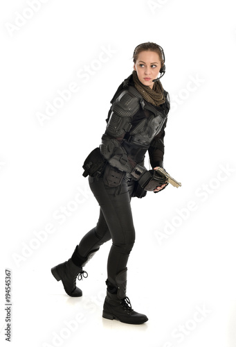 full length portrait of female soldier wearing black tactical armour, holding a gun, isolated on white studio background.