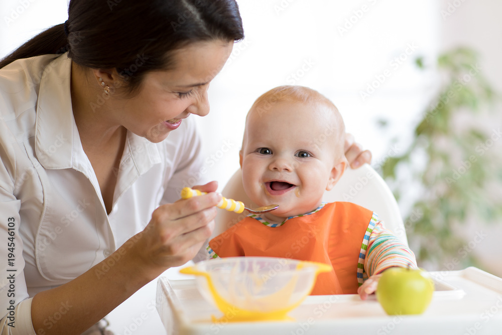 Mom giving homogenized food to her baby son on high chair. Mom giving homogenized food to her baby son on high chair.