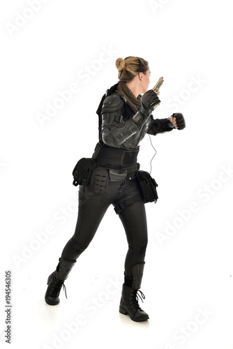 full length portrait of female soldier wearing black tactical armour, holding a gun, isolated on white studio background.