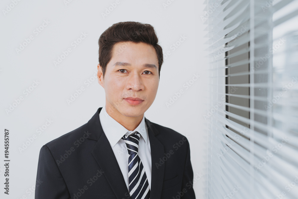 Smiling asian businesman standing by the window. Smiling asian businesman standing by the window.