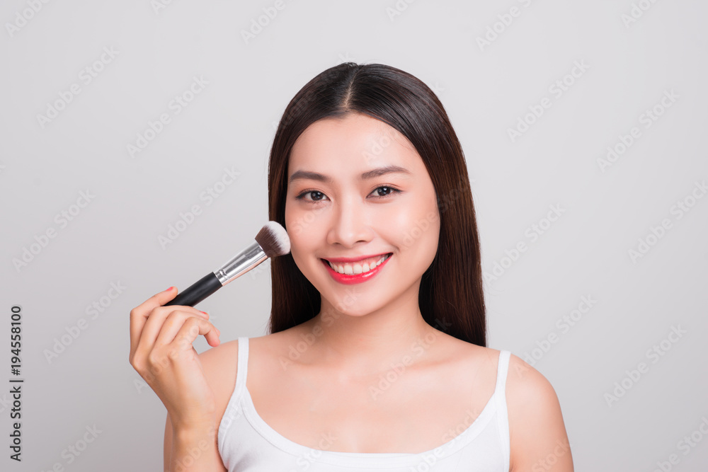 Beautiful young asian woman with perfect skin applying makeup with a brush Beautiful young asian woman with perfect skin applying makeup with a brush