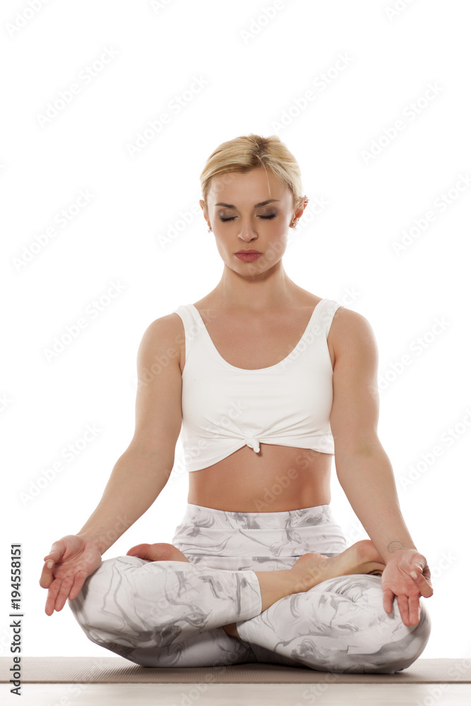 Yoga, sport, training and lifestyle concept - Young blonde woman doing yoga exercise. Portrait of young beautiful woman in white sportswear doing yoga practice. Lotus pose. Yoga, sport, training and lifestyle concept - Young blonde woman doing yoga exercise. Portrait of young beautiful woman in white sportswear doing yoga practice. Lotus pose.
