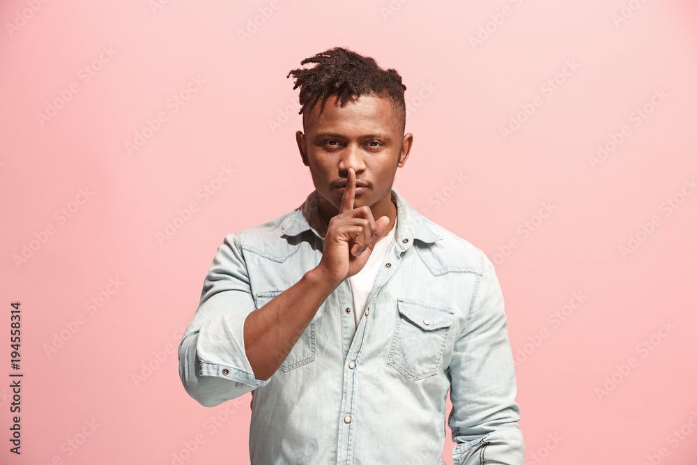 The young man whispering a secret behind her hand over pink background The young man whispering a secret behind her hand over pink background