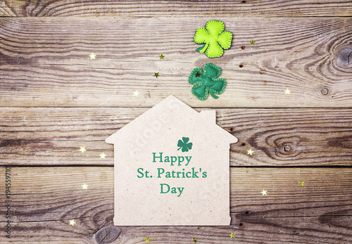 St.Patrick's day greeting message with lucky home symbol and four-leaf clover on wooden background.