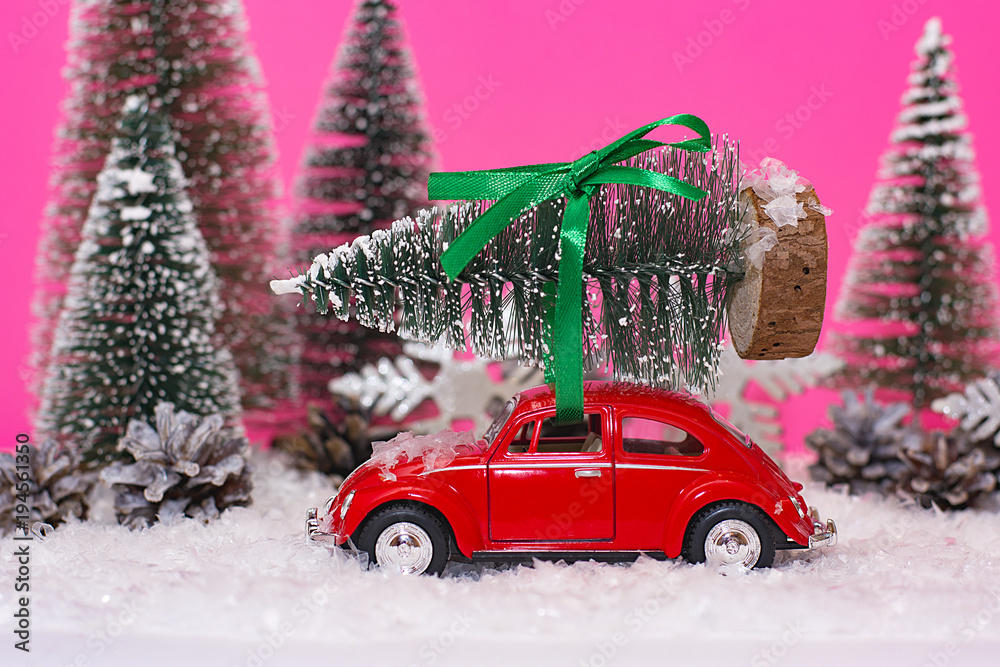 Car carrying a Christmas tree in a snow covered miniature evergreen forest