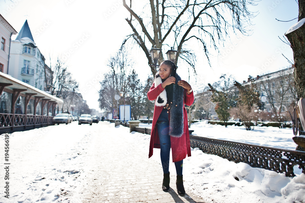 Rich african american girl in red coat and fur on winter street at sunny weather. Black stylish woman.