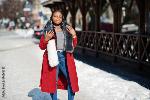 Rich african american girl in red coat and fur on winter street at sunny weather. Black stylish woman.